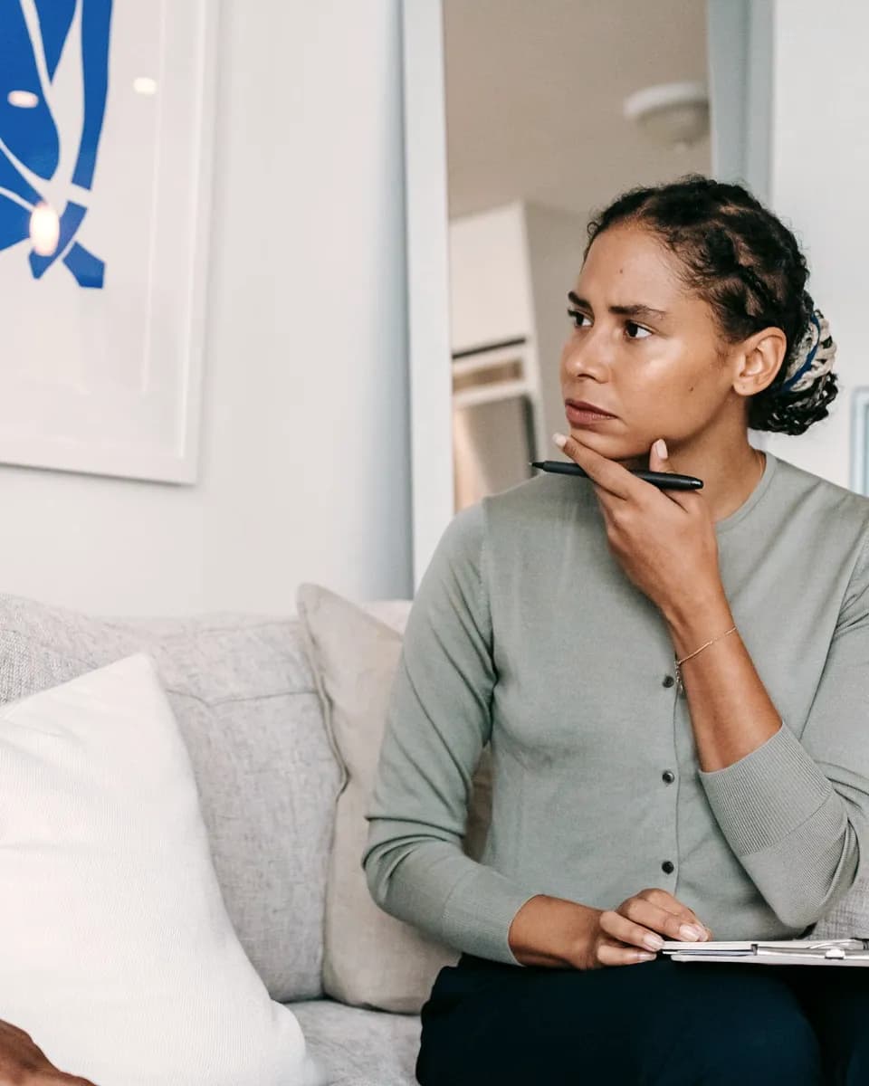 A man on a sofa speaking with his counsellor, who listens with a clipboard