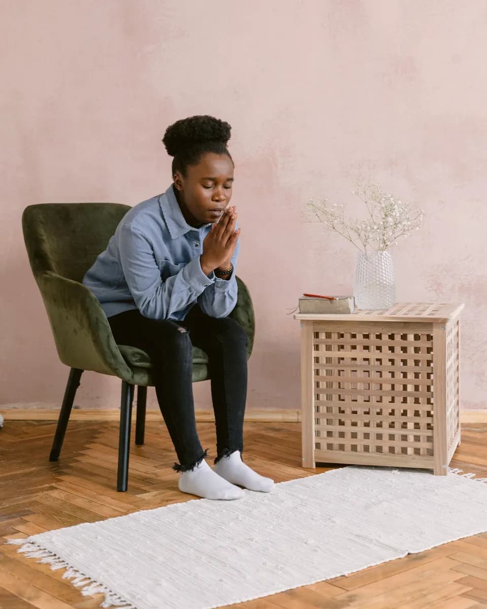 Someone sits quietly in a green armchair, feet on a rug beside a book on a side table