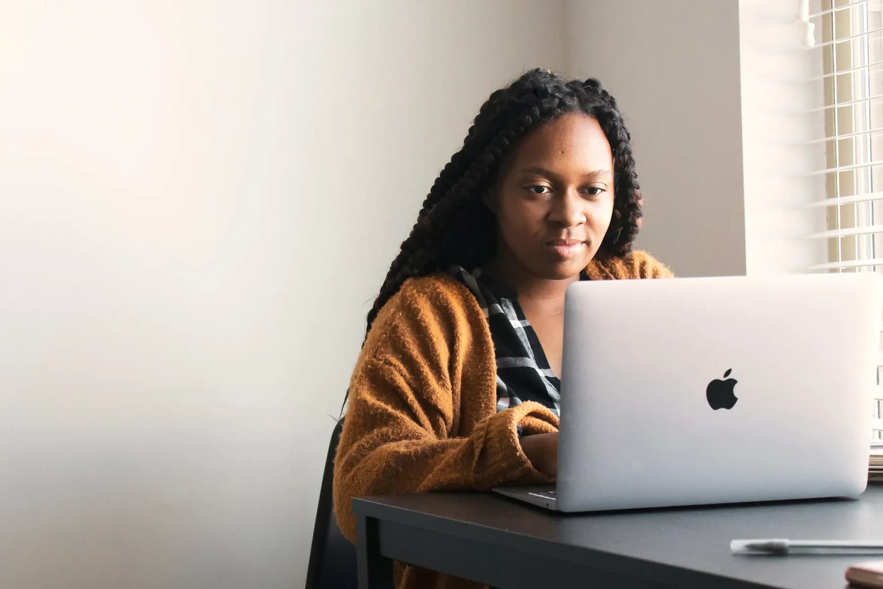 A woman with long braids sitting at a laptop in a calm, bright room